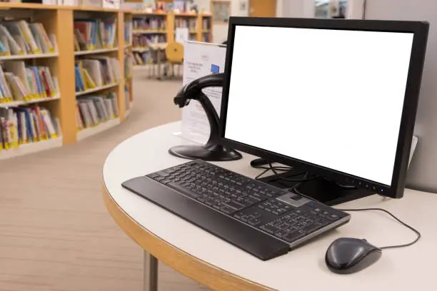Photo of Computer with blank screen monitor on table in interior library