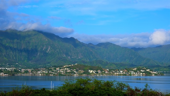 Kaneohe town as viewed from across Kaneohe Bay with Ko'olau mountains in background.  A few sailboats moored in the bay.