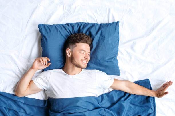 istock Bedtime. Guy lying on bed top view waking up stretching closed eyes smiling toothy 1177944428