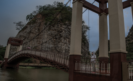 Young asian woman standing on a Wood bridge walkway over the swamps on a rainy day.