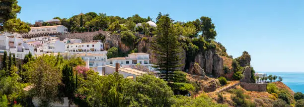 Luxury villas and green trees located on rock against cloudless blue sky on coast of sea on sunny day on resort in Mijas, Malaga, Costa del sol, Spain.