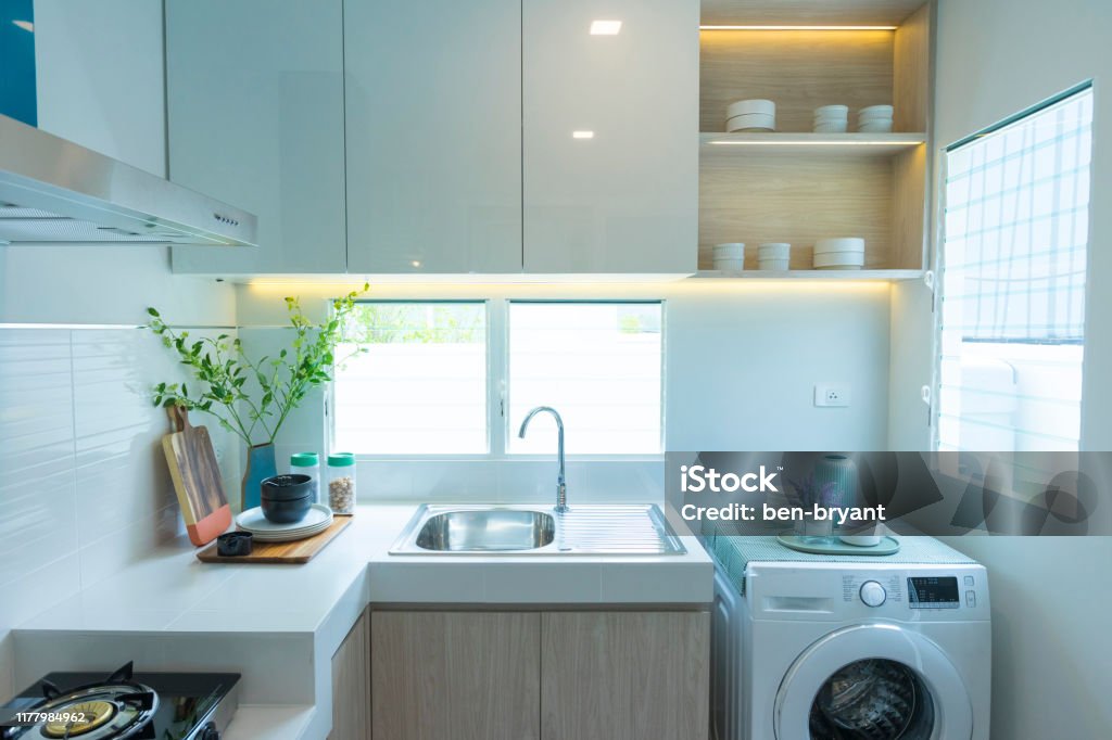 Modern kitchen counter with washing machine and cooking stove by the window. Modern kitchen counter with washing machine and cooking stove by the window at home. Apartment Stock Photo