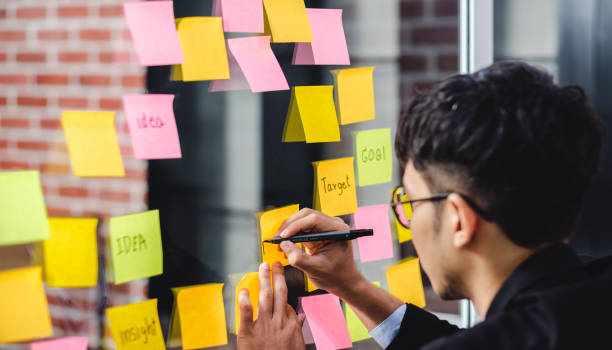 istock asian businessman looking and writing on sticky note for brainstorming ideas on clear whiteboard at modern office. analyse and synthesis 1177992900