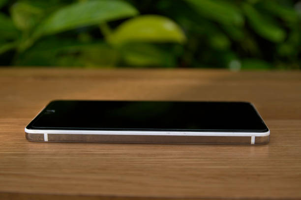 istock Smart phone lying on a table with a dark green leafy eco background mockup 1177994374