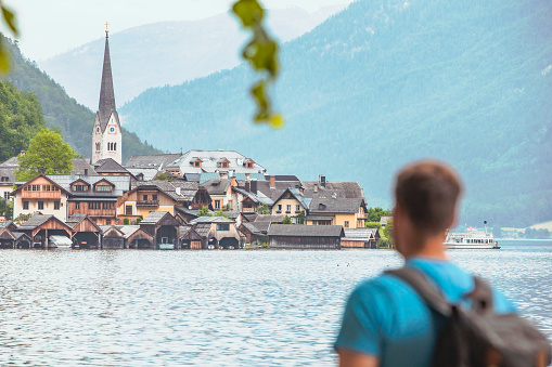 man traveler backpacker looking at hallstatt town at other side of the lake summer time