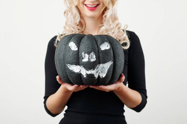 Foam plastic pumpkin painted with white and black as jack-o-lantern in hands of smiling young woman