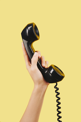 Hand of person holding black telephone receiver