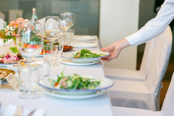 A close up of the waitress hand serves the salad dish on the banquet table stock photo