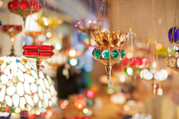 Colorful electric lamps arranged on glass shelves. Illuminated lanterns for sale in market. Cables are wrapped around them.