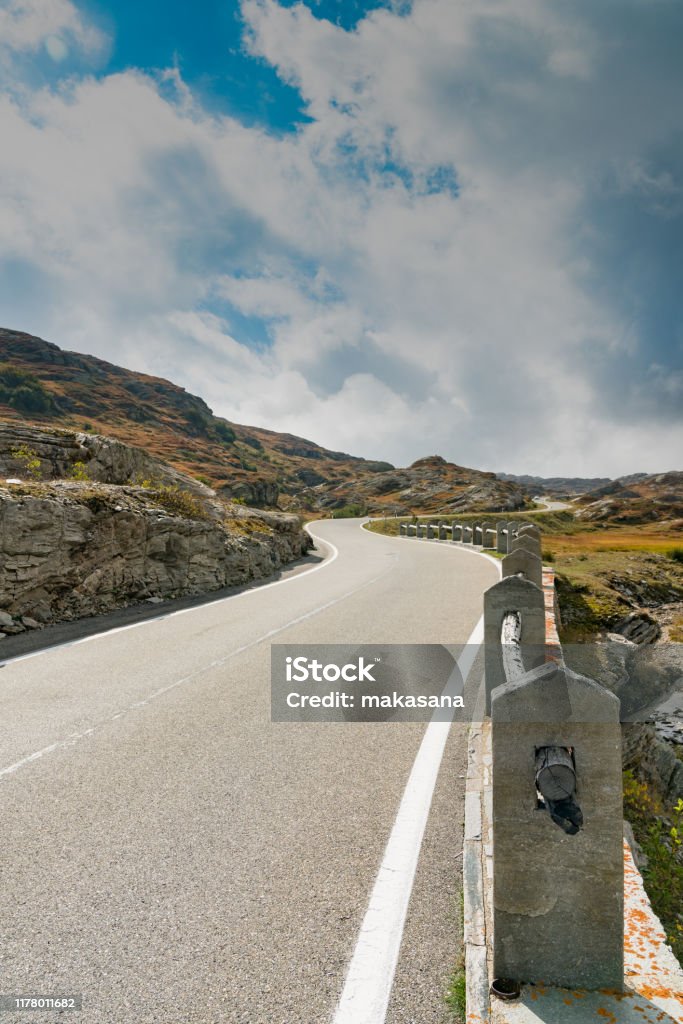 vertical view of a two-lane road leading over a high remote and wild mountain pass in the Swiss Alps A vertical view of a two-lane road leading over a high remote and wild mountain pass in the Swiss Alps Alpine climate Stock Photo
