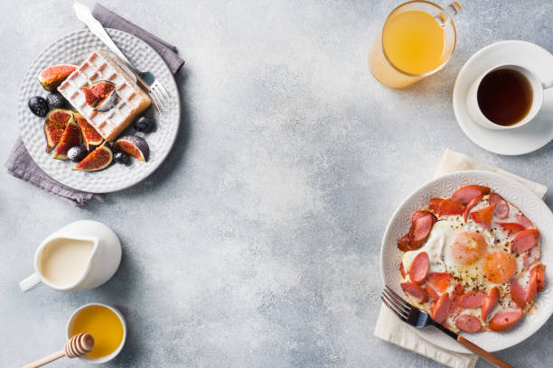 istock Dishes for home cooked hearty Breakfast. Fried eggs with sausages and tomatoes. Belgian fluted waffles with figs and grapes. Gray concrete background copy space. 1178011983
