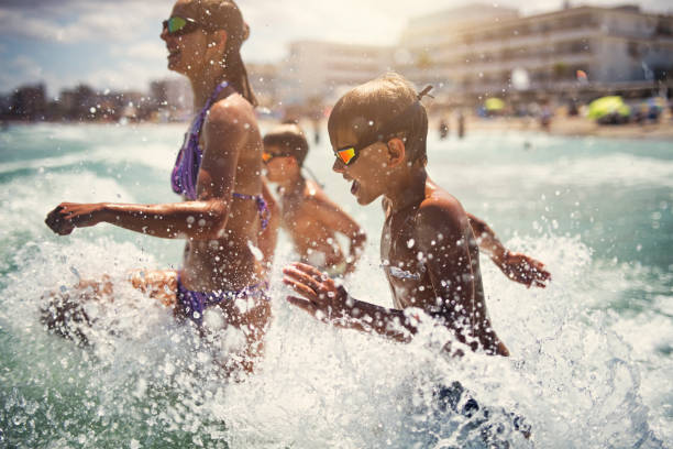 Brothers and sister are having fun in sea waves. Kids are running into incoming waves and laughing.Sunny summer day evening.Nikon D800