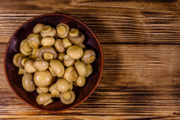 Ceramic plate with canned mushrooms on rustic wooden table. Top view