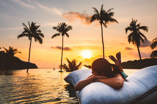 Summer vacation concept, Silhouette asian woman with bikini relax in infinity pool hotel resort with sea beach and palm tree background at sunset in Koh Kood, Thailand