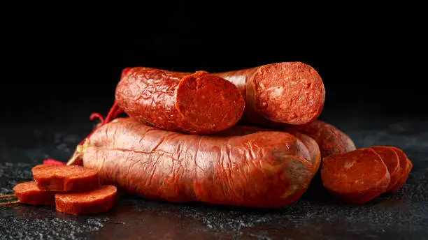 traditional Balearic raw cured meat sobrassada sausage made from ground pork, paprika and spices on rustic black background.