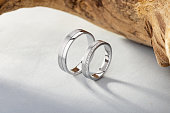 Pair of silver wedding rings with diamonds on gray background with wood