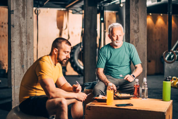 istock Active elderly man eating a healthy, protein-rich, chicken salad meal together with his personal trainer in a gym gym 1178043108