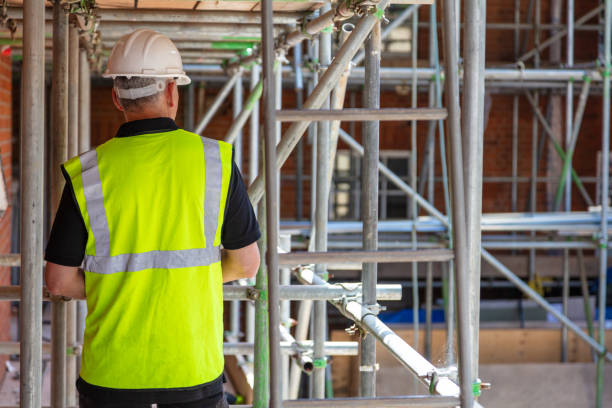 Rear view of male builder construction worker contractor on building site wearing hard hat and hi-vis yellow vest stock photo