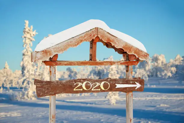 Photo of 2020 written on a wooden direction sign, blue sky and winter snowy tree landscape background happy holiday seasons new year greetings