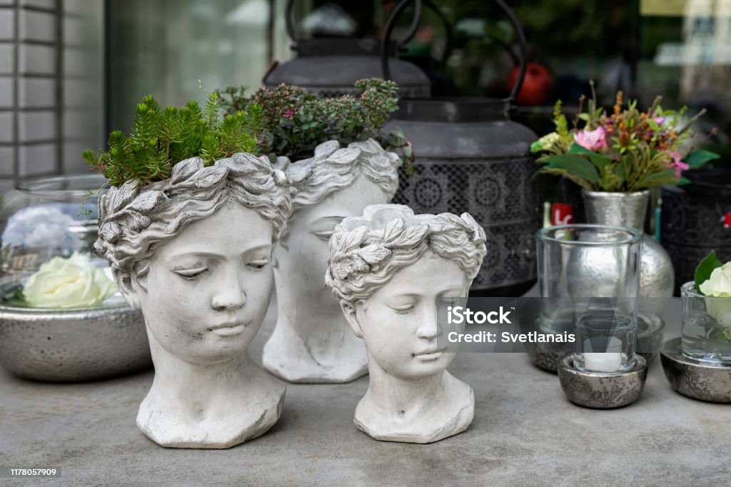 Gypsum flower pot in the shape of antic head of goddess with growning out green flowers. Stylish home decor Gypsum flower pot in the shape of antic head of goddess with growning out green flowers. Creative home decor Vase Stock Photo