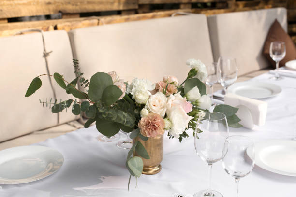 istock Wedding table setting decorated with fresh flowers in a brass vase. Wedding floristry. Banquet table for guests outdoors with a view of green nature. Bouquet with roses, eustoma and eucalyptus leaves 1178058706