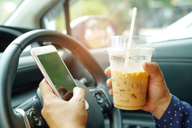 signora asiatica che tiene il caffè ghiacciato e il telefono cellulare in auto per comunicare con gli amici in vacanza calda felice. - driving foto e immagini stock