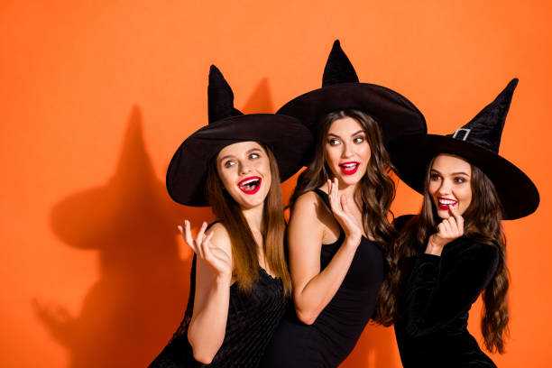 photo de trois dames cruelles de sorcière appelant les mecs beaux utilisant des pouvoirs magiques paranormal portent des robes noires et des chapeaux de magicien le fond orange de couleur d'isolement - sensuality halloween witch devil photos et images de collection