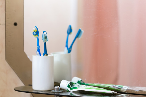 Two old toothbrushes and an old toothpaste lie on a shelf in the bathroom.