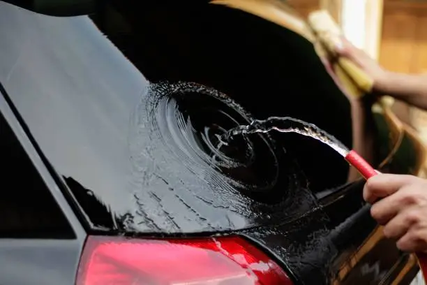 Man washes a black car with a hose. Self-car wash. Close up.