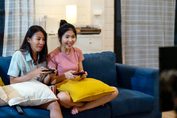 szczery młodych azjatyckich kobiet lub przyjaciół grających w gry wideo śmiejąc się szczęśliwy i siedzi na kanapie wraz z zabawy i copyspace. konkurs gry młodych azjatyckich dziewcząt przyjaciół lub siostry rodziny. - video game friendship teenager togetherness zdjęcia i obrazy z banku zdjęć