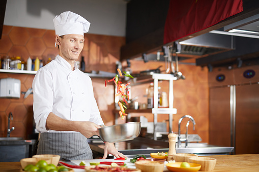 Waist up portrait of handsome chef tossing vegetable while cooking Asian dish in restaurant kitchen, copy space
