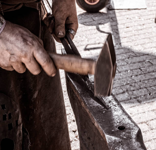 istock A blacksmith working outdoors on a small anvil, striking the hammer down on what they're currently working on 1178076644