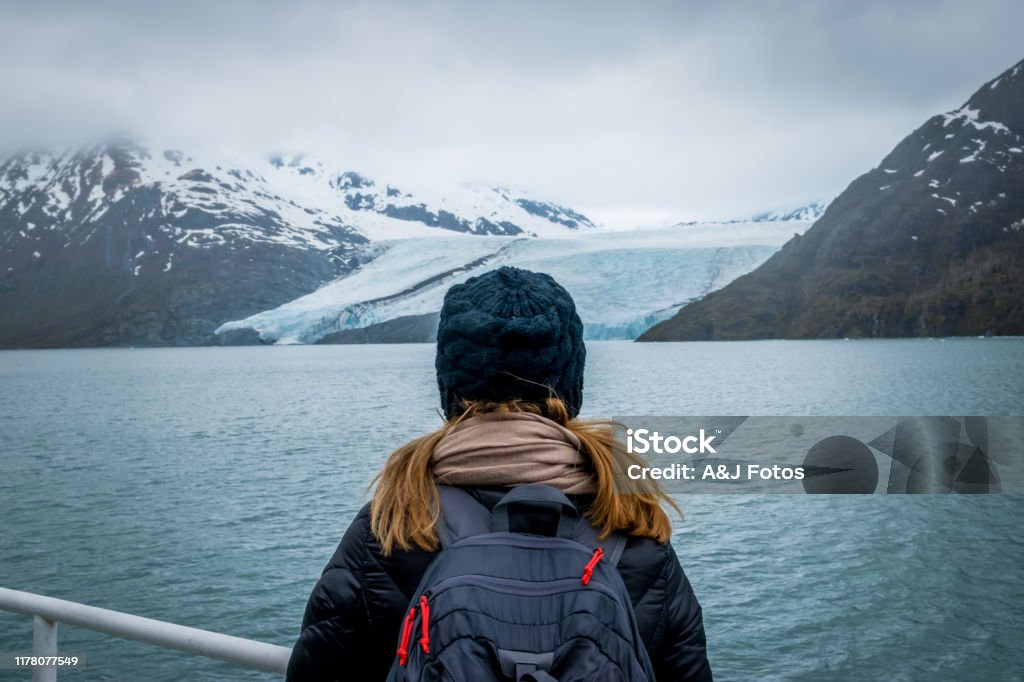 Woman looking at mountain range and glacier. Woman doing a cruise and looking at the Portage glacier in Alaska with snowcapped mountains in background. Alaska - US State Stock Photo
