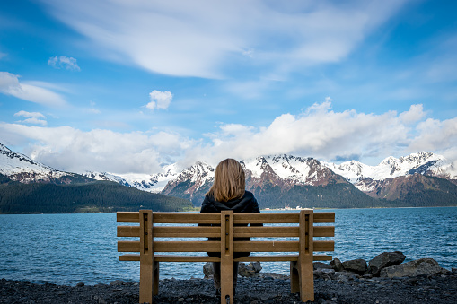 Woman looking at the Resurrection Bay by the city of Seward, Alaska, with snowcapped mountains in background.