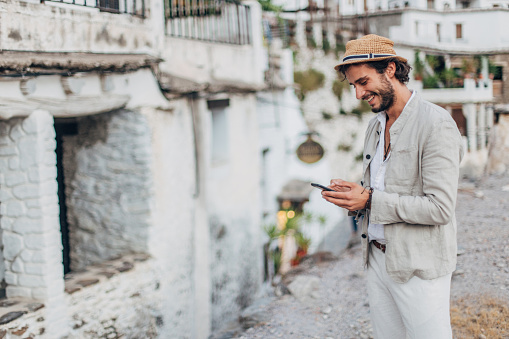 Handsome hipster man texting on mobile phone in some Spanish village