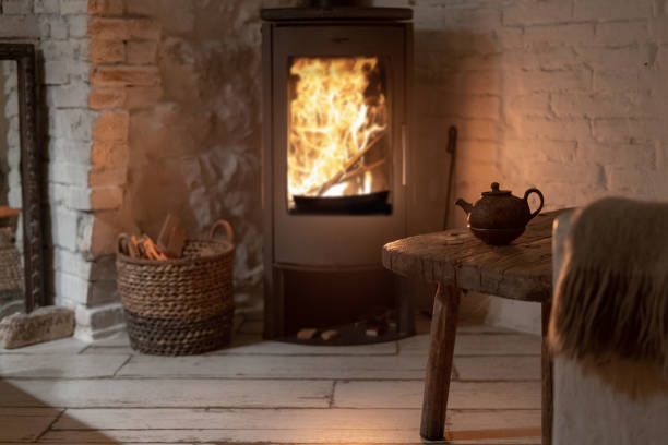istock Selective focus on table and ceramic teapot against wood stove fireplace with fire on blurred background. Wicker basket with firewood near chimney in comfort house with cozy interior in room 1178085336