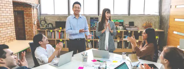Millennial boss team leader introducing New asian woman employee to colleagues in creative office workplace. Welcoming hired newcomer member to team. first work day get clapping hands with colleagues.