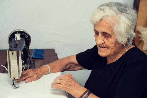 A woman in her 80s sitting on her antique sewing machine, working.