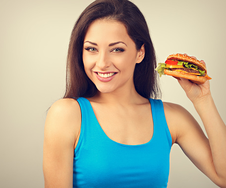 Funny smiling hungry excited woman holding in the hand the burger and looking on blue background. Closeup toned vintage portrait