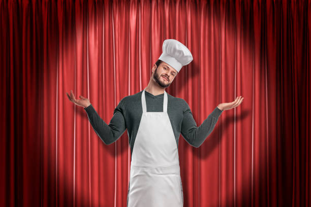 istock Chef wearing kitchen apron and chef hat holding hands up on red stage curtains background 1178092428