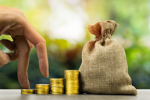 Making money and money investment, Savings concept. A man hand on rising stack of coins with money bag and nature background. Depicts long-term investment And wealth and financial stability.