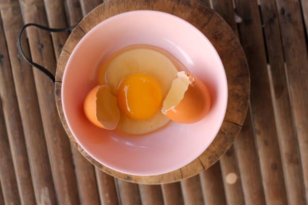 istock shell with egg and open Eggs in a pink bowl Placed on the butcher on Bamboo battens.Top view closeup. 1178095525