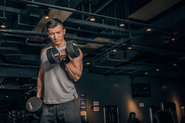 Fit Chinese guy practicing with dumbbells in gym
