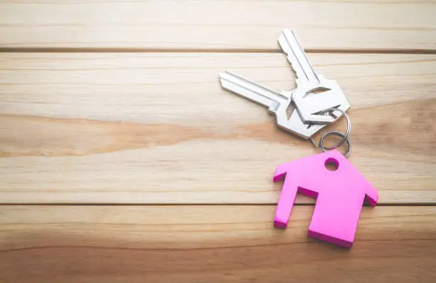 House key on a house shaped keychain concept, moving home or renting property, planning savings money of coins to buy a home concept for property, mortgage and real estate investment for a house.