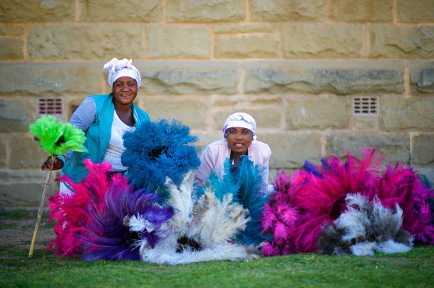 Two Ostrich Feather Sellers sitting with feather dusters looking away Two Friendly African women portrait selling Ostrich Feather Multi coloured vibrant Dusters in Oudtshoorn Klein Karoo South Africa ostrich farm stock pictures, royalty-free photos & images