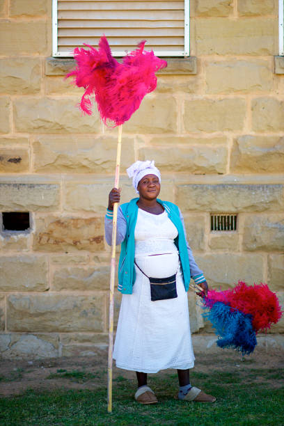 Ostrich Feather Seller Full Length standing proudly alone Friendly African woman portrait selling Ostrich Feather Multi coloured vibrant Dusters in Oudtshoorn Klein Karoo South Africa ostrich farm stock pictures, royalty-free photos & images