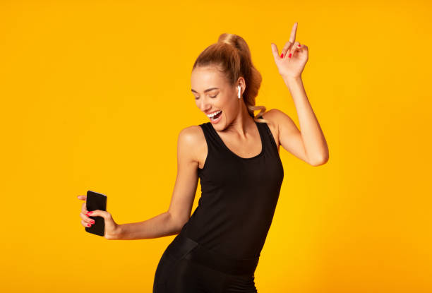 istock Young woman holding smartphone dancing on yellow studio background 1178127315
