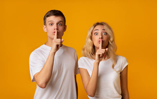 istock Young couple holding fingers on lips and looking at camera 1178129015