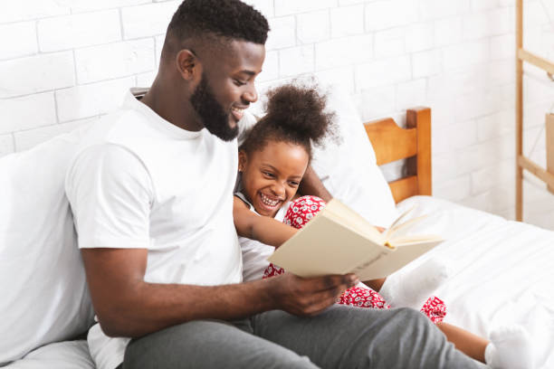 loving african american dad reading fairy tales to his little daughter - sleeping child bedtime little girls imagens e fotografias de stock