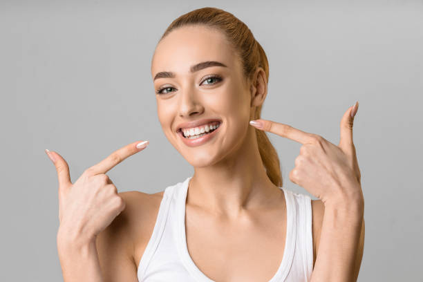 Orthodontic concept. Happy girl showing her beaming white teeth Orthodontic concept. Happy girl showing her beaming white teeth with two forefingers, grey background perfection stock pictures, royalty-free photos & images